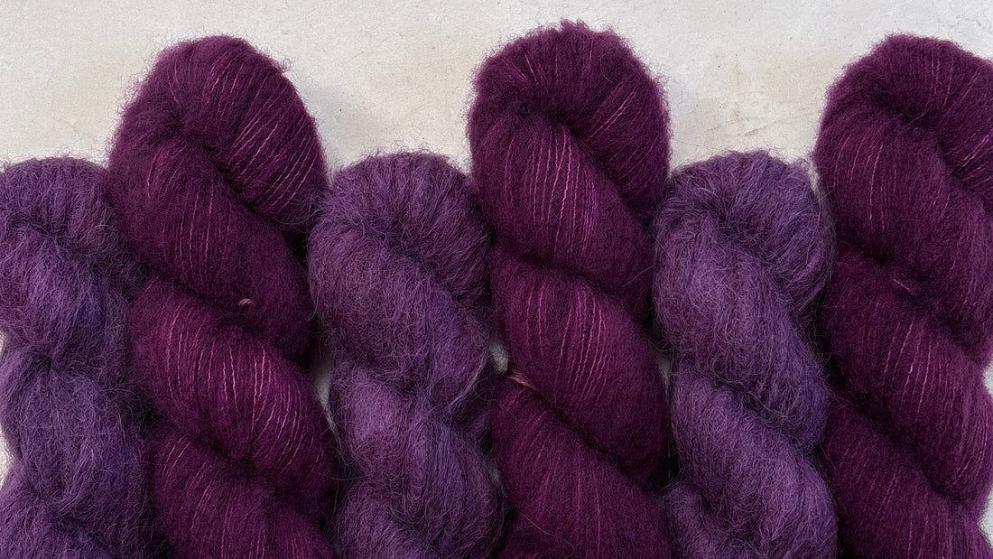 Hand dyed skeins of fluffy yarn sitting on a light stone background.