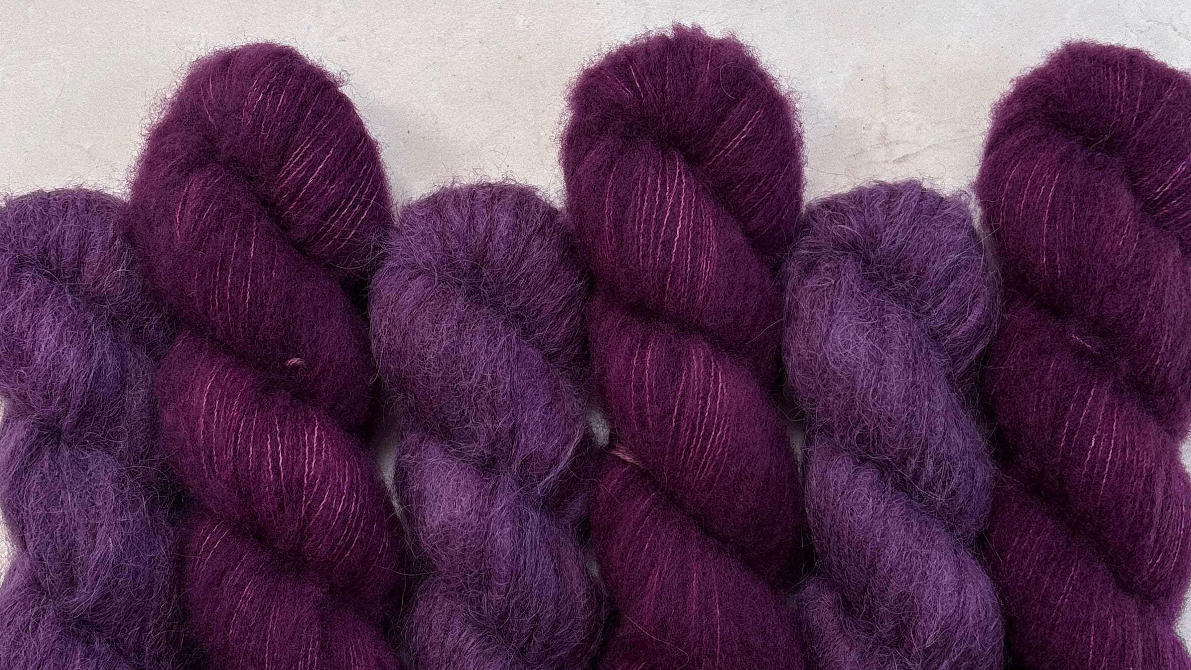 Hand dyed skeins of fluffy yarn sitting on a light stone background.