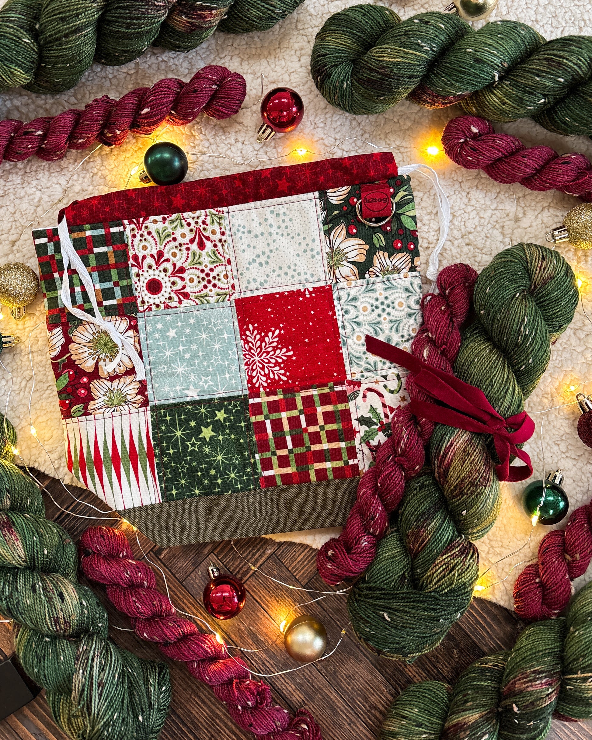 Colorful yarn skeins and a patchwork fabric on a wooden surface with festive lights.